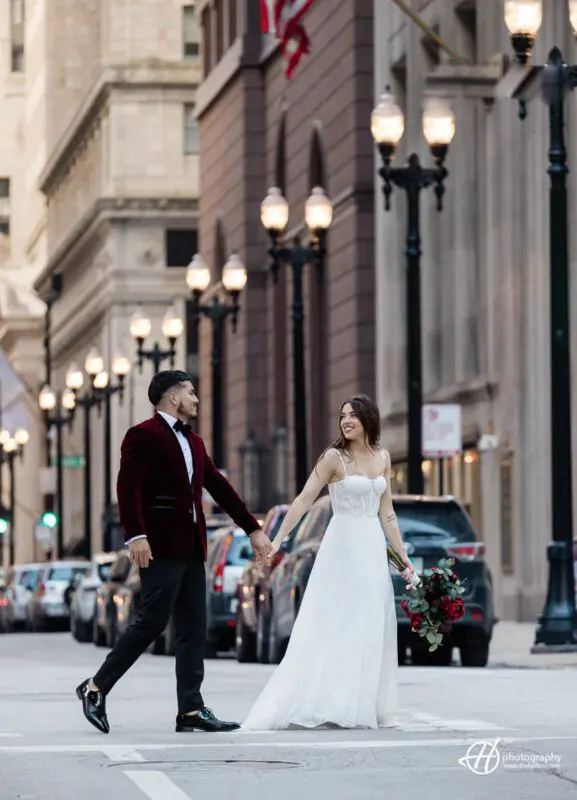 Samuel and Faith take a stroll in front of the iconic Chicago Board of Trade building, surrounded by bustling city streets. They walk hand in hand, with Samuel carrying a backpack and Faith holding a coffee cup. The towering building behind them is a symbol of Chicago's financial history and architectural beauty.