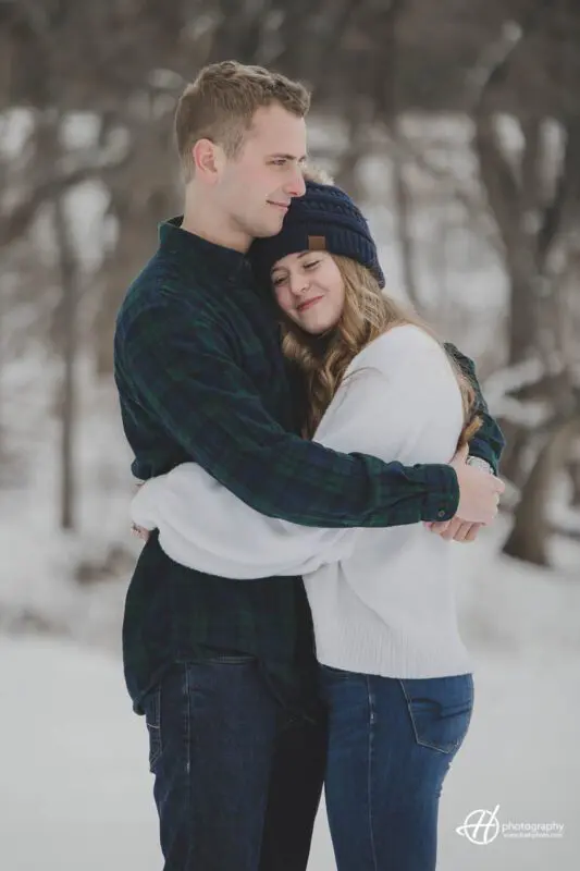 A couple embraces in a loving hug during their engagement photo shoot, with the sun setting behind them and casting a warm glow on their faces. 