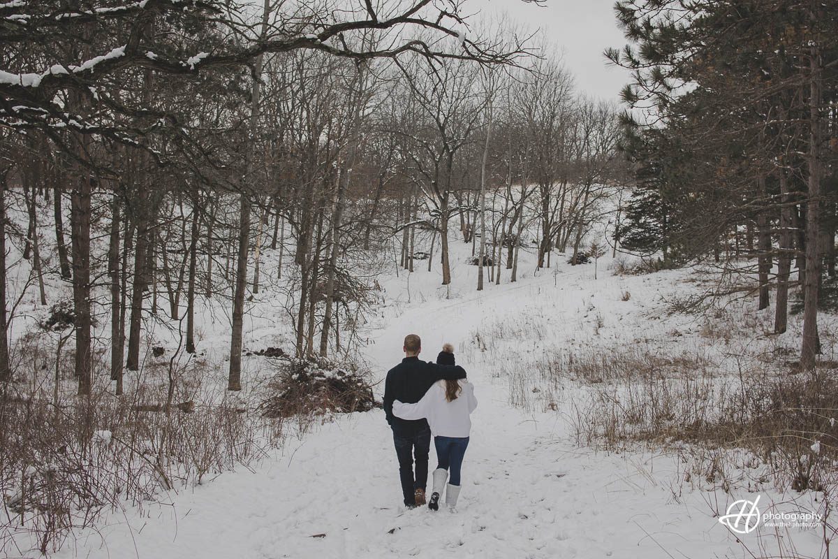 2 / 2 Image of the couple walking together in the snow during their engagement session at Veteran Acres in Crystal Lake, IL, enjoying the winter scenery and each other's company.